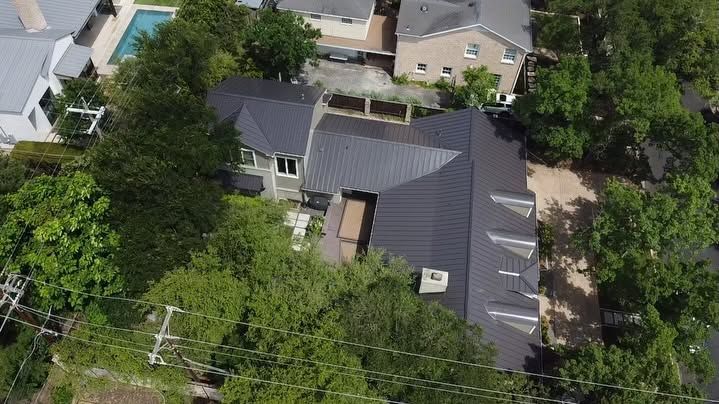 Aerial view of a gray-roofed house surrounded by trees and neighboring homes.