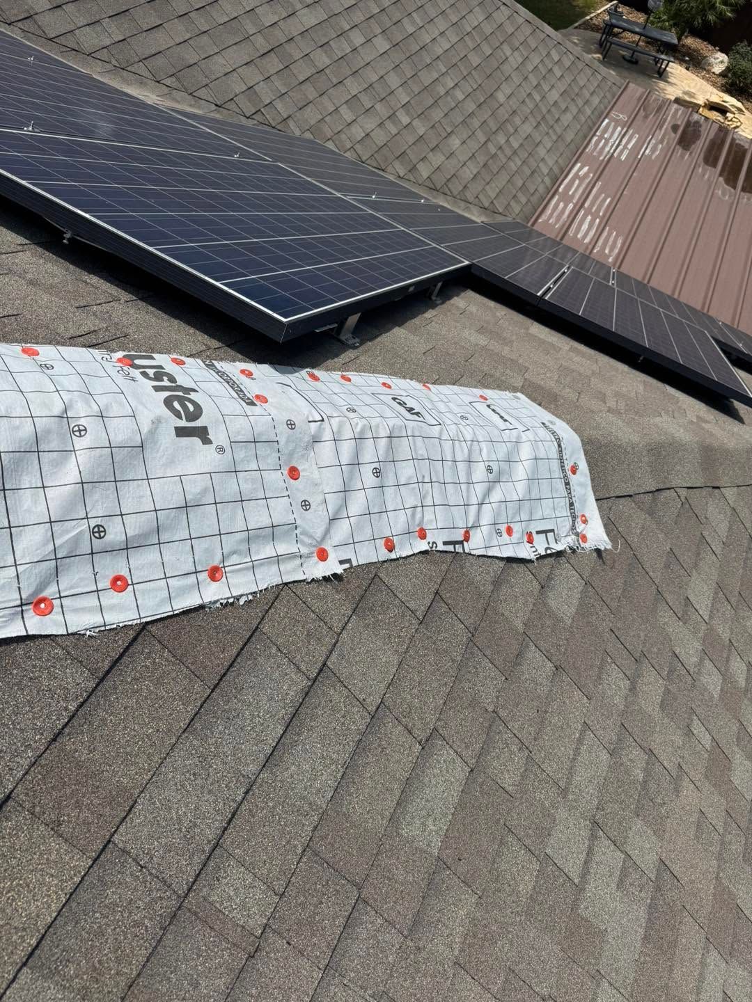 Solar panel and a roof patch covered with white material on a shingled rooftop.