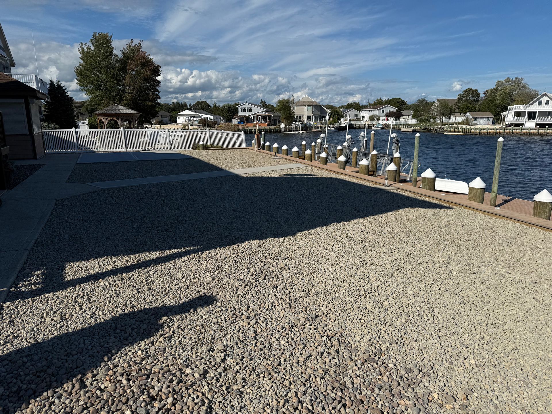 Rocky waterfront path with white railings, boats, and houses under a blue sky