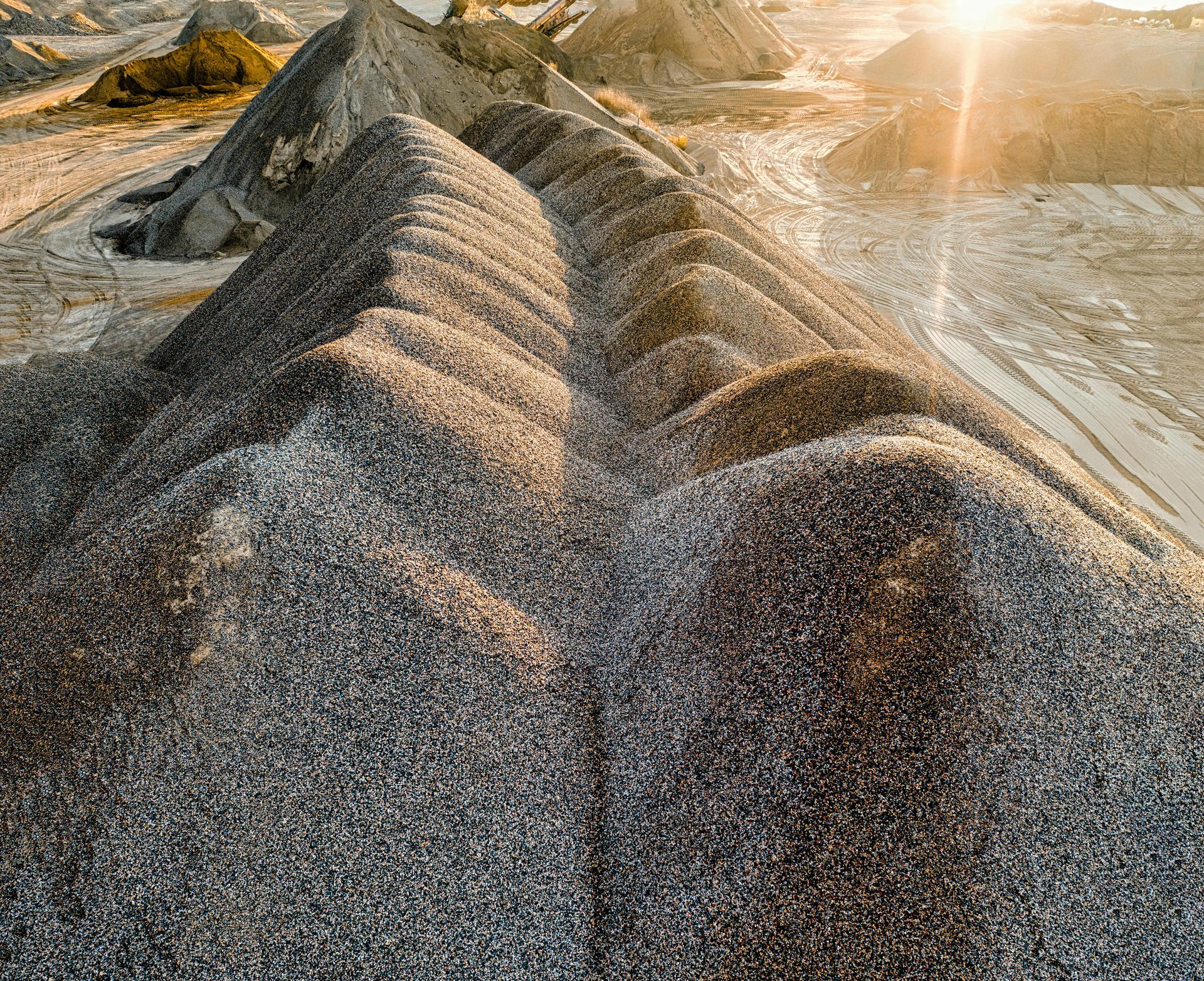 Sunlit gravel piles with a sharp ridge in a dusty quarry landscape