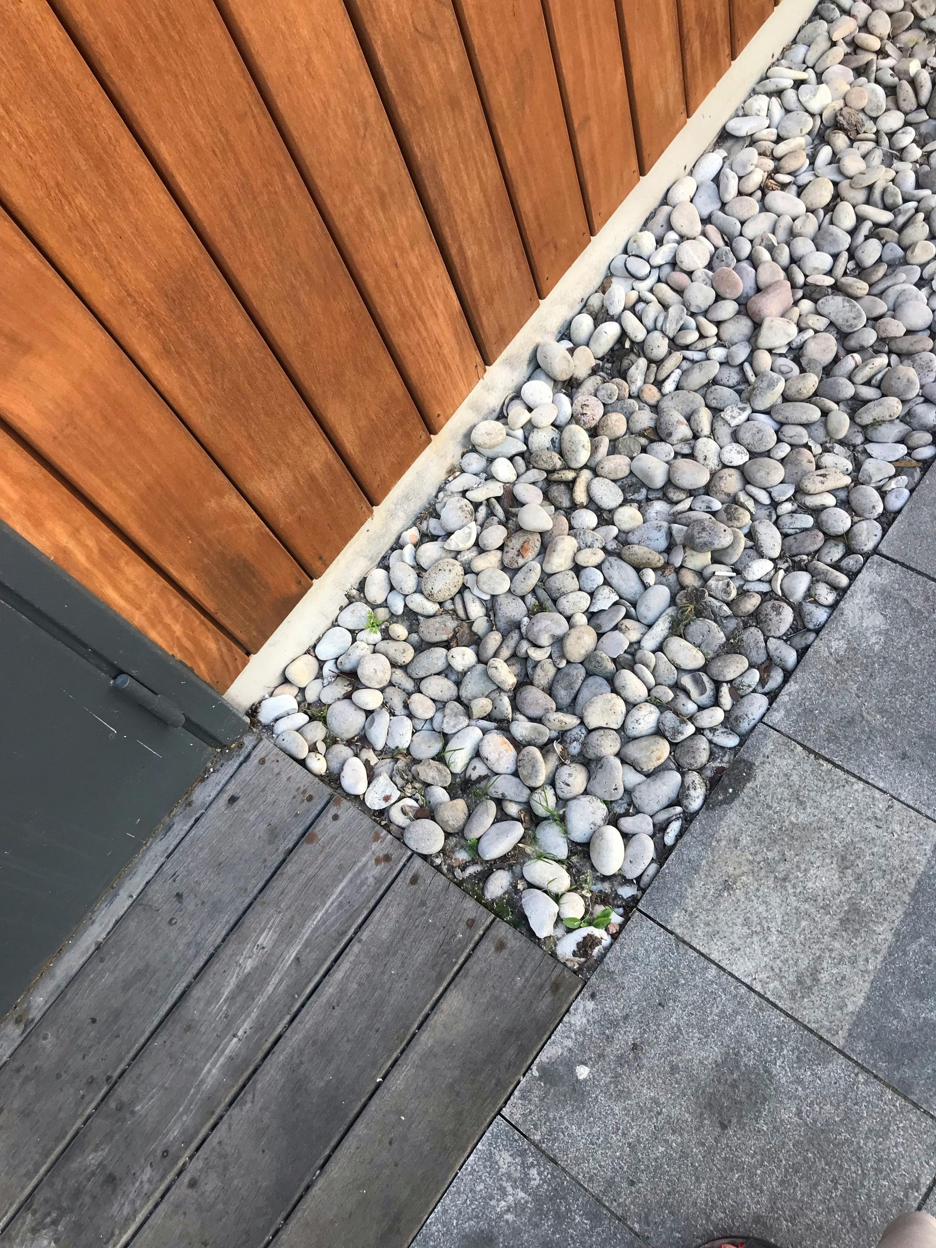 Wooden fence corner beside gray pebbles and dark deck and patio paving