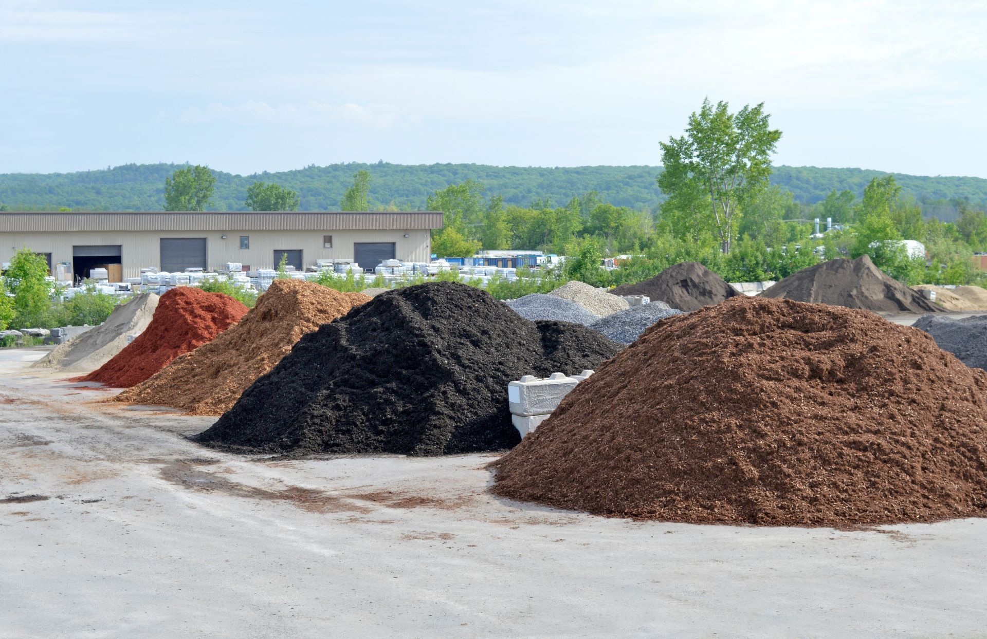 Piles of mulch and gravel in a yard with trees and hills in the background