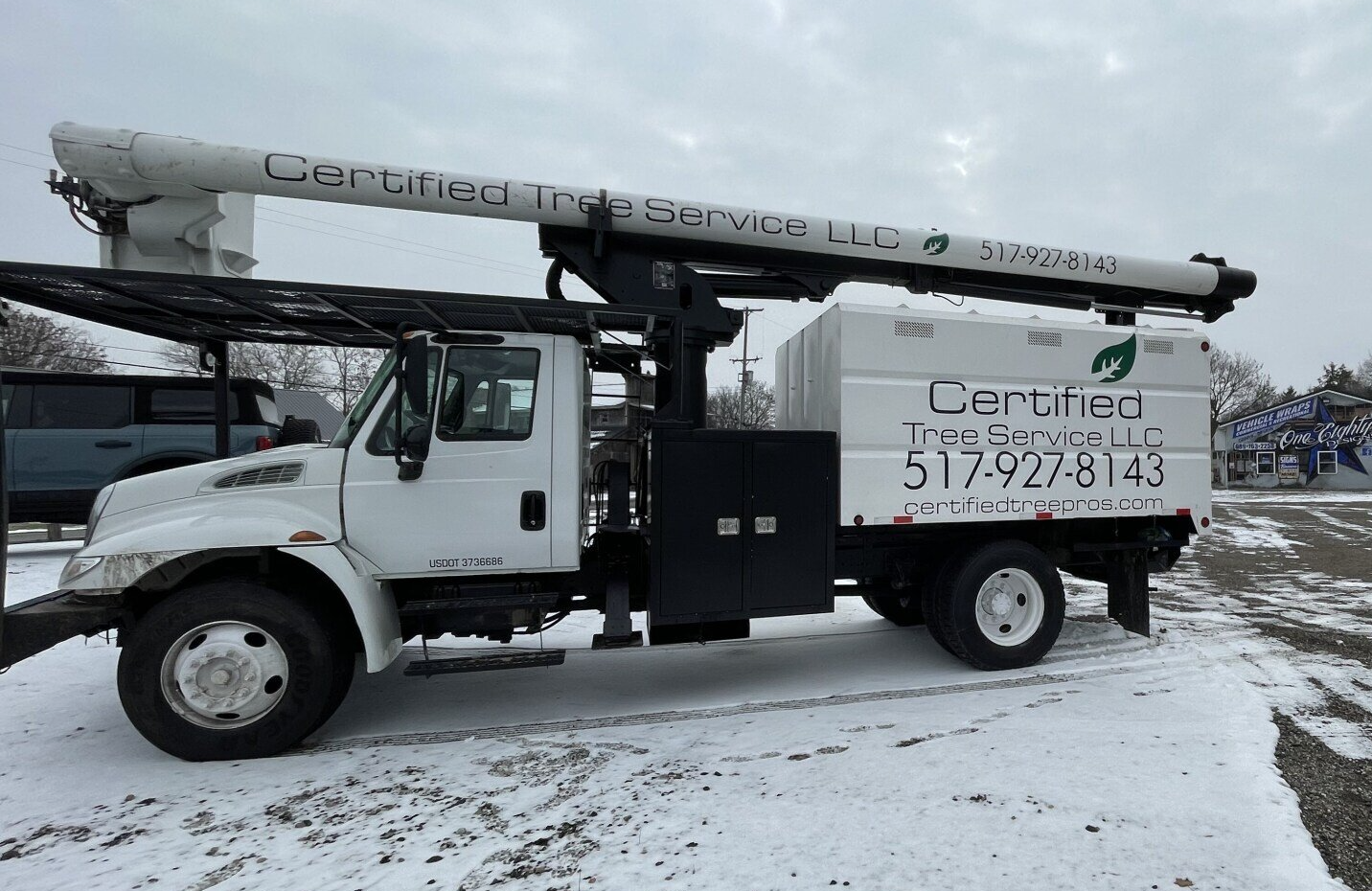 A white truck with a crane on top of it is parked in the snow.