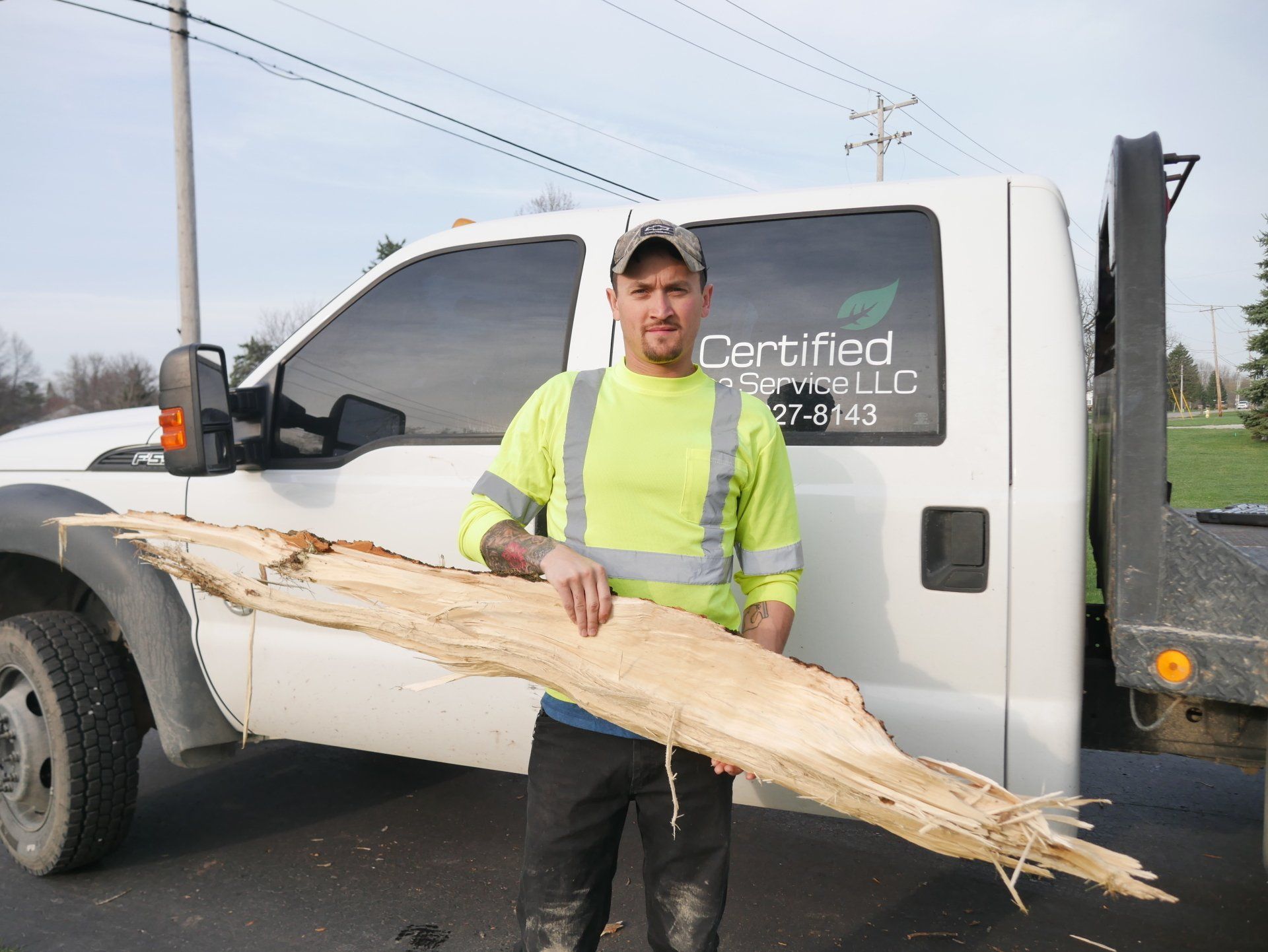 A man is holding a large piece of wood in front of a certified truck