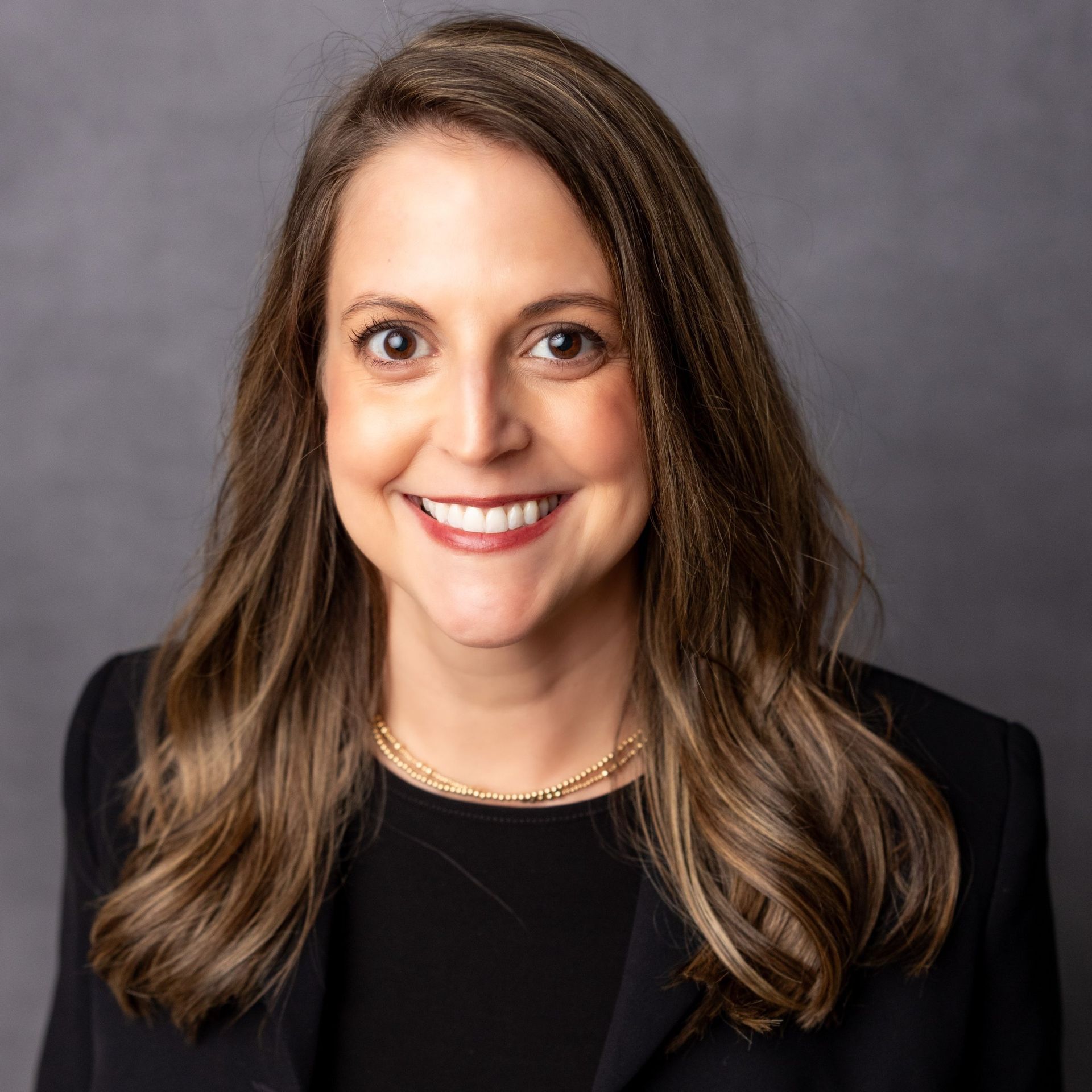 A woman wearing a black jacket and a necklace is smiling for the camera.