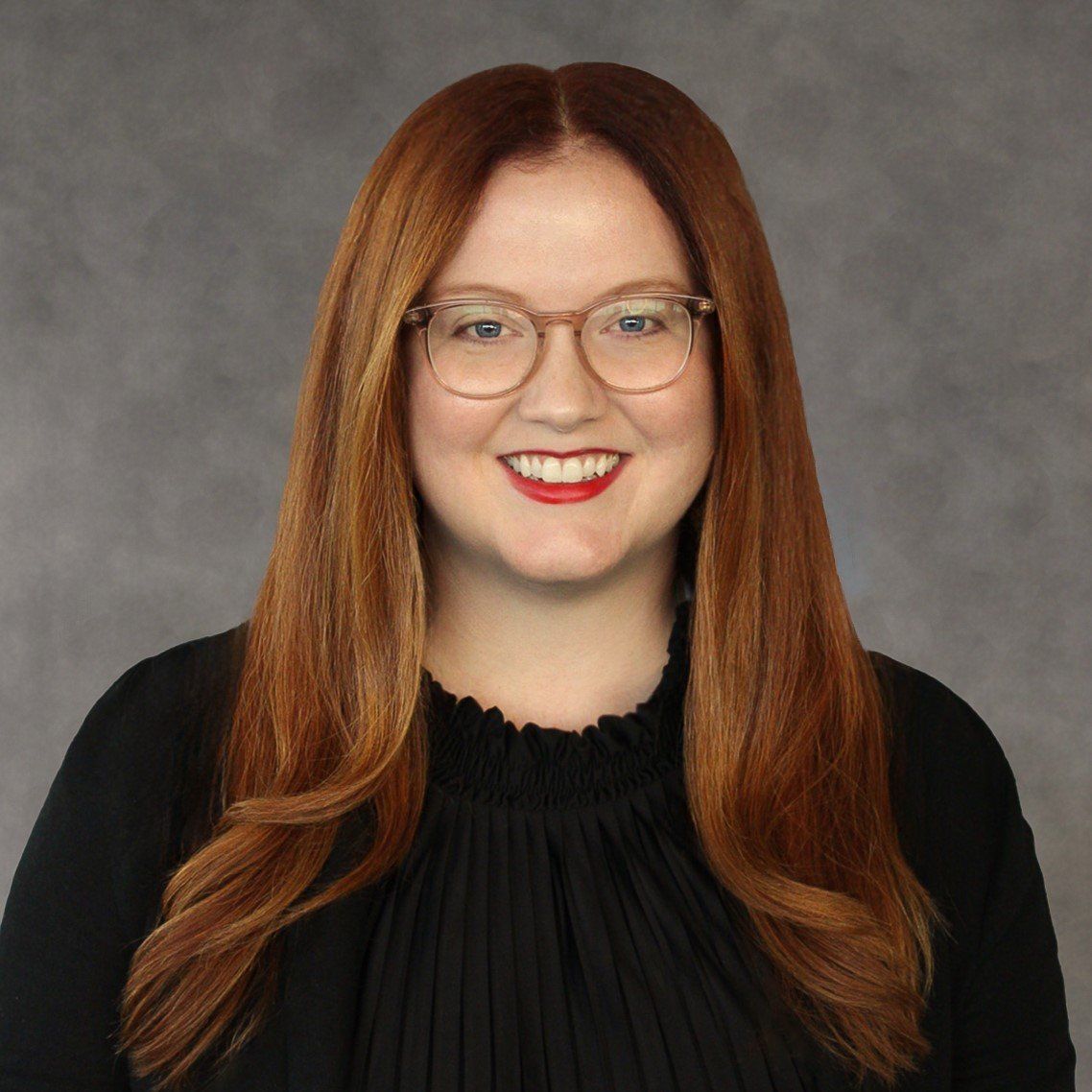 A woman wearing glasses and a black shirt is smiling for the camera.