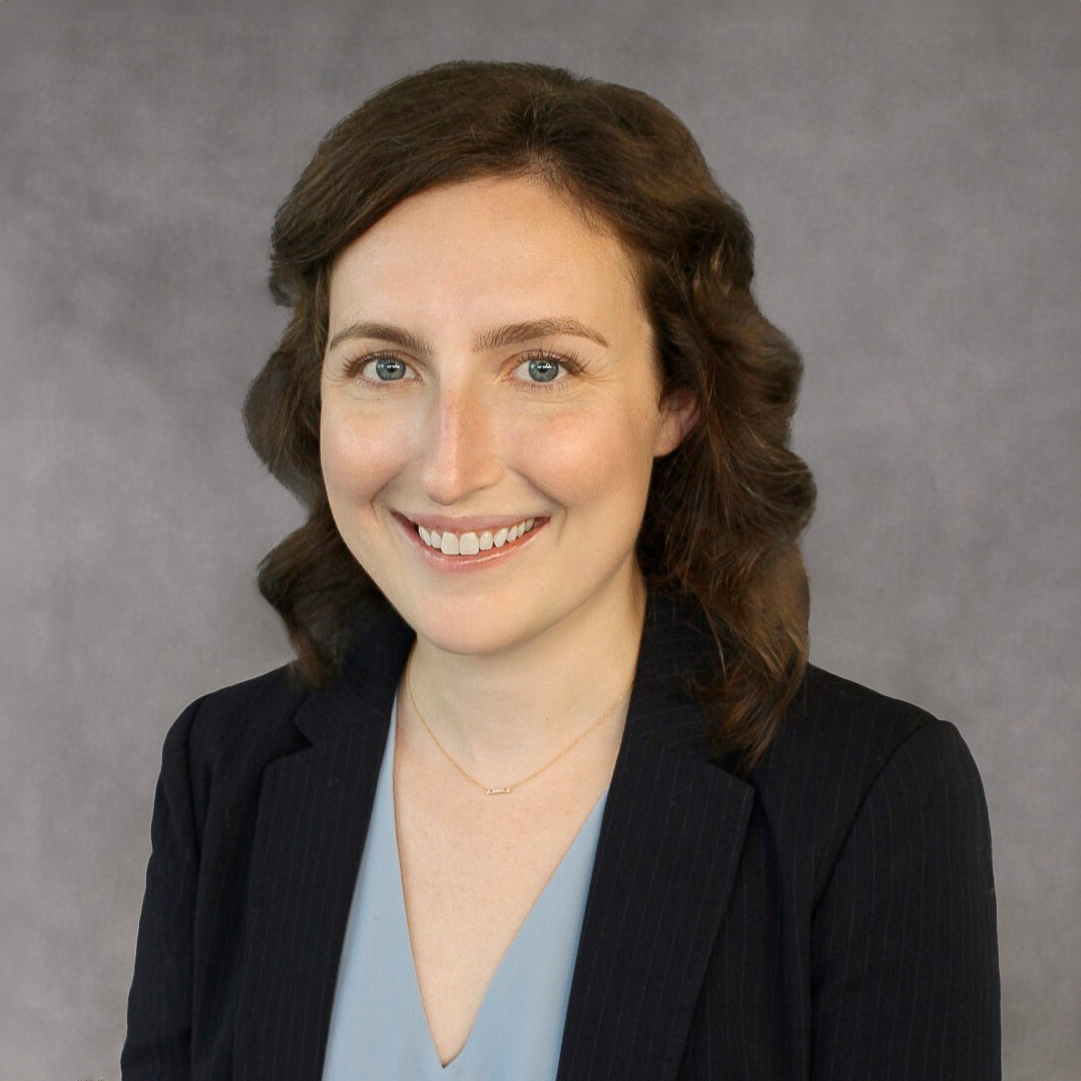 A woman wearing a blue shirt and a black jacket is smiling for the camera.