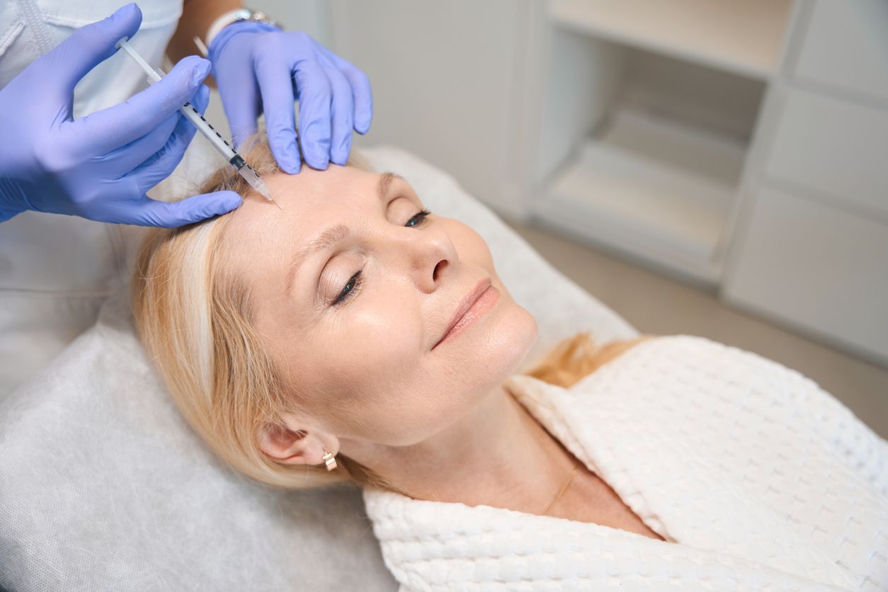 A woman is getting a botox injection in her forehead.