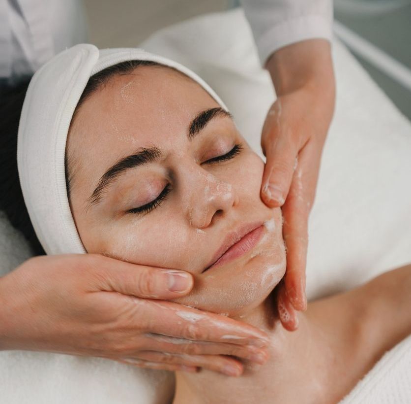 A woman is getting a facial massage with her eyes closed