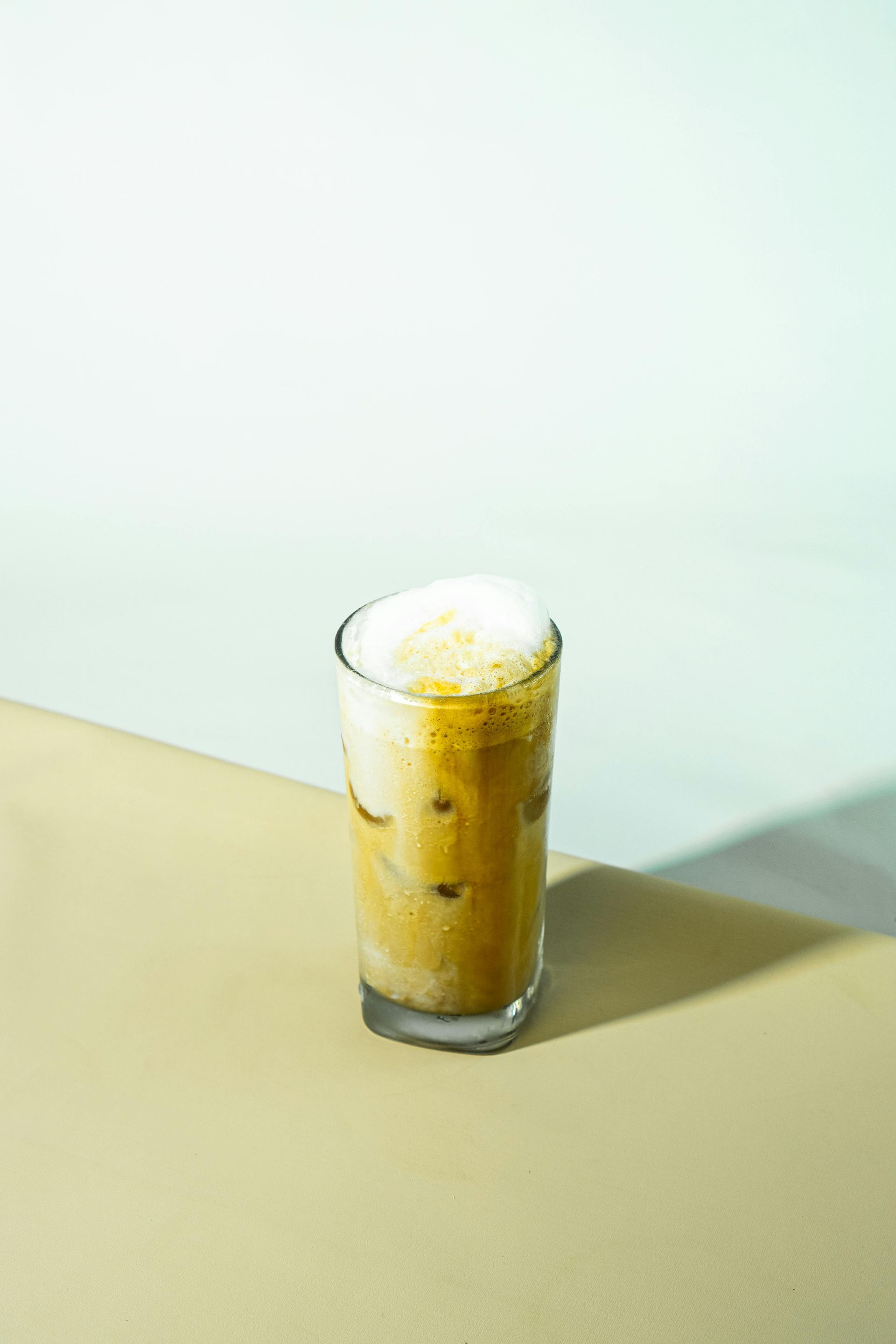 Iced coffee in a tall glass, set against a two-tone background of light brown and pale green.