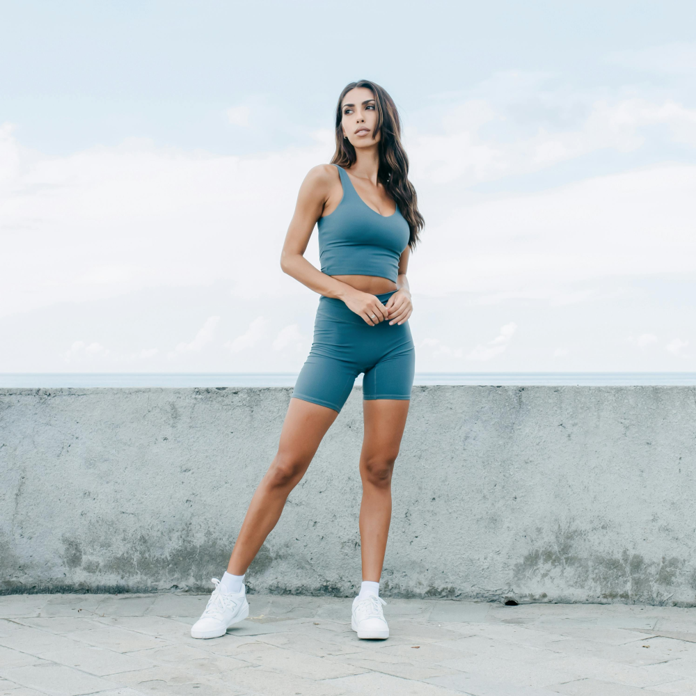 Woman in blue athletic shorts and crop top, posing with hands on hips.