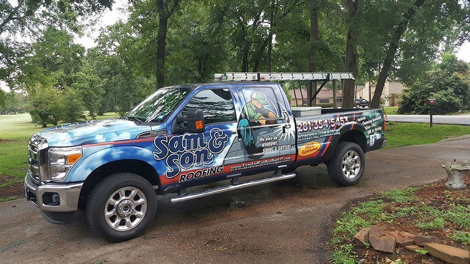 Blue and silver pickup truck with company logo, parked on a driveway, carrying a ladder.