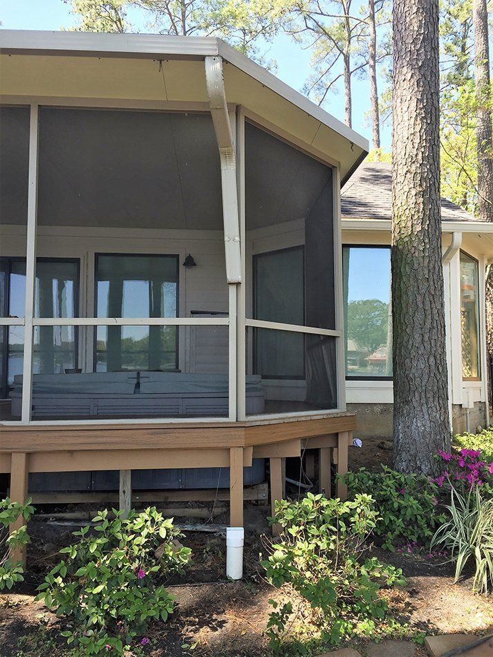 Screened-in porch on a house with a wooden deck, next to a large tree and landscaping.