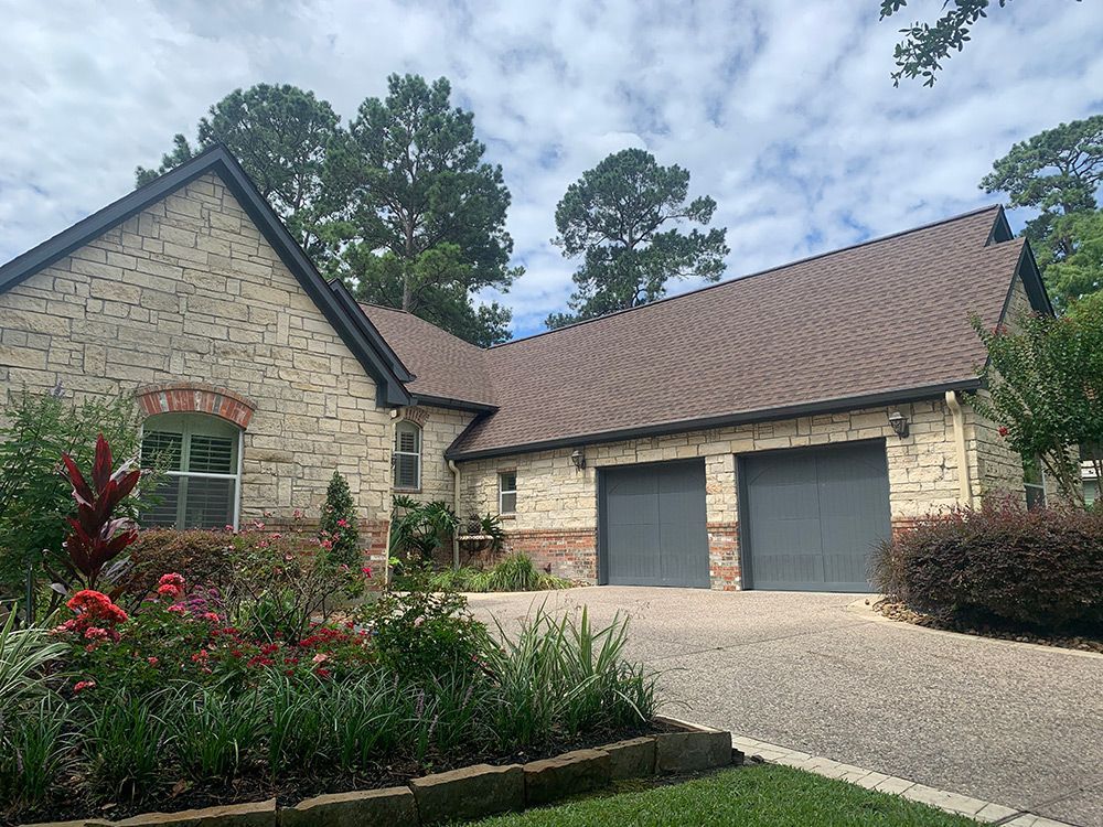 Light brick house with brown roof and gray garage doors; flower beds in the front.