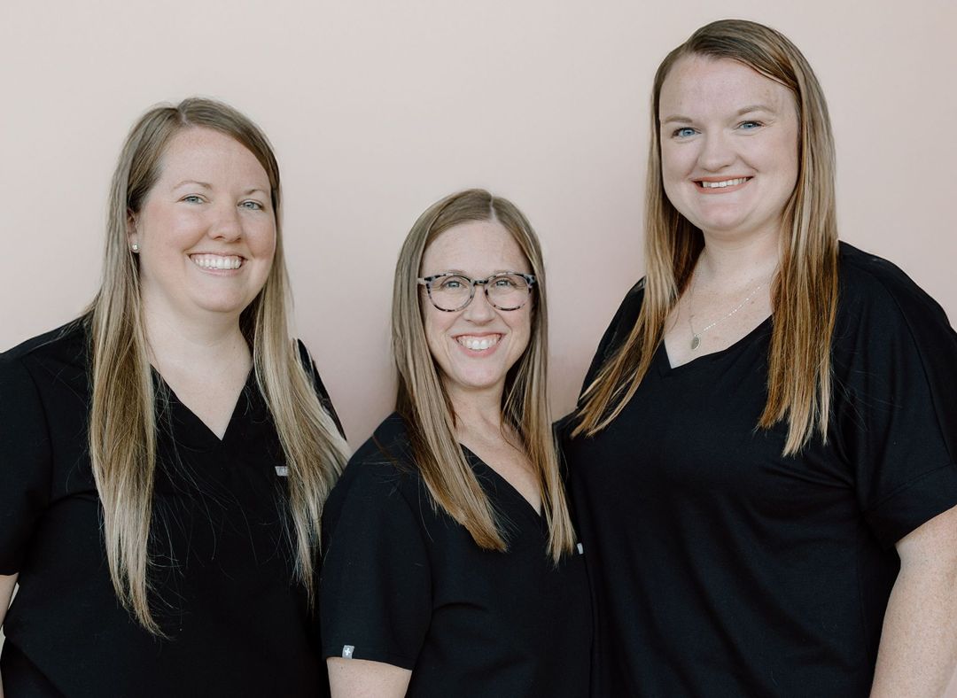 Three smiling people in black tops, standing in front of a pink wall.