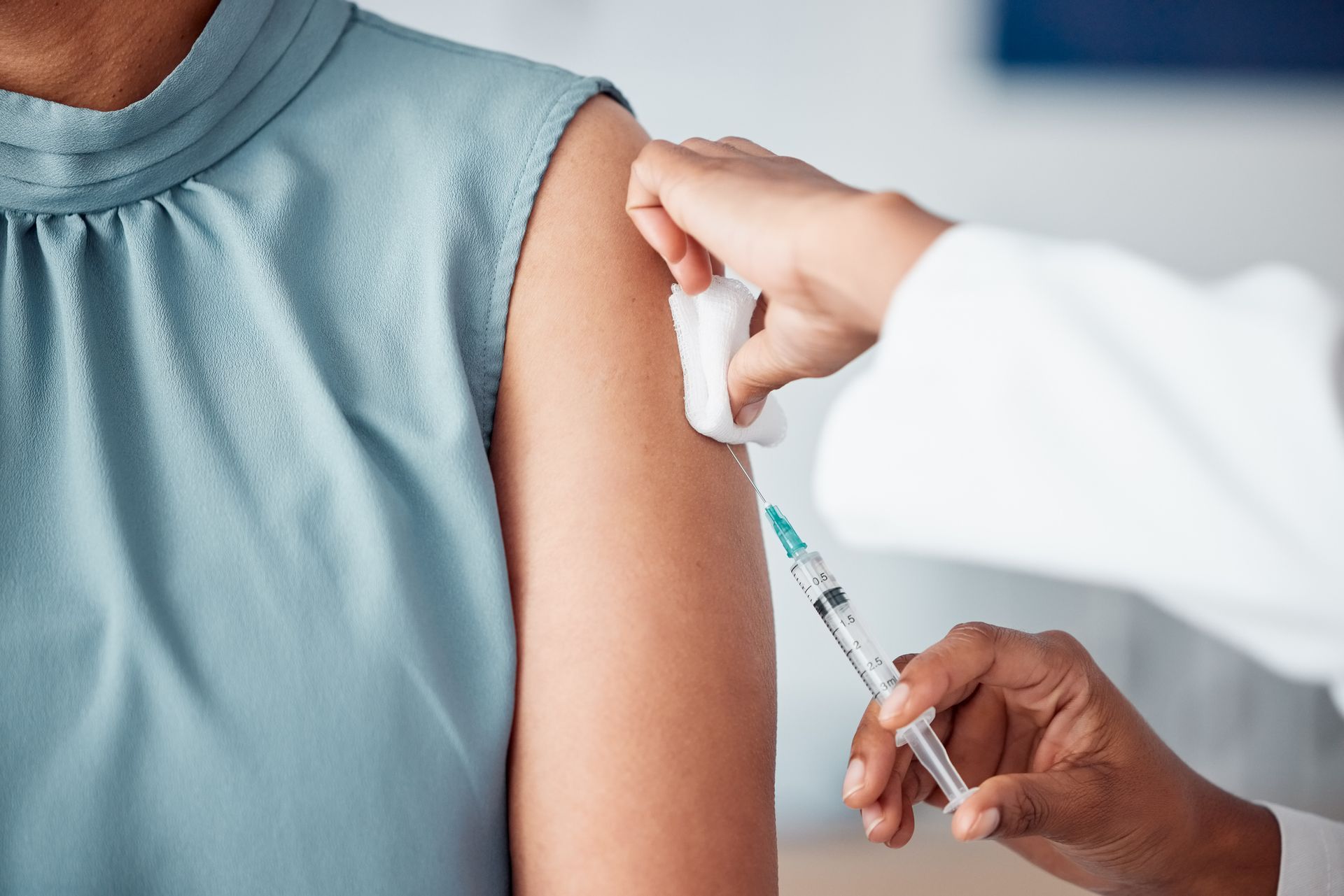 Person receiving an injection in the upper arm from a person in a white coat; medical setting.