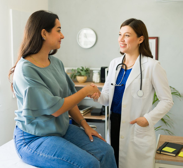 Woman shaking hands with a doctor in a medical examination room; both smiling.