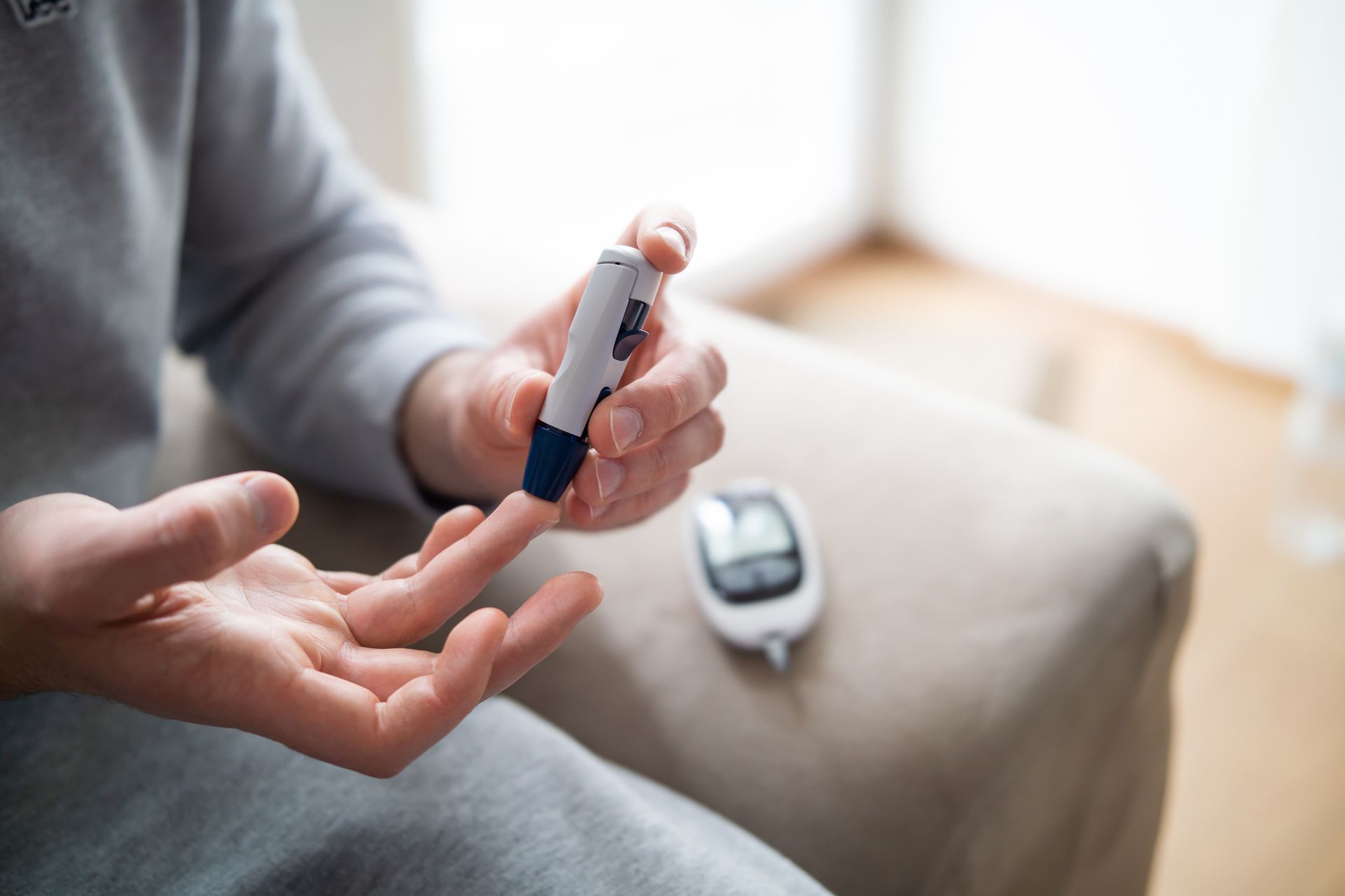 Person using a blood glucose meter to test their finger, indoors.