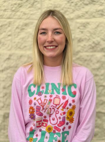 Smiling woman in a pink floral graphic T-shirt standing against a beige stone wall