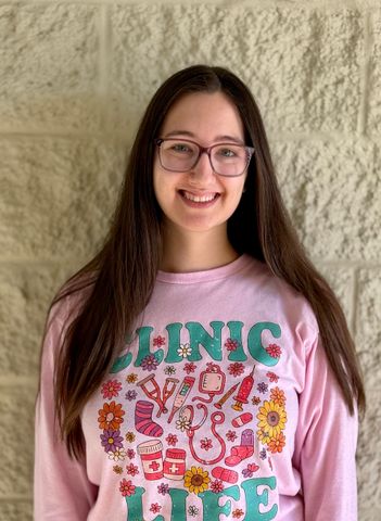 Smiling woman in a pink floral graphic T-shirt standing against a beige stone wall