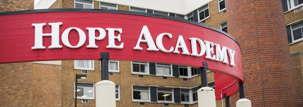 A red sign that says hope academy is in front of a brick building.