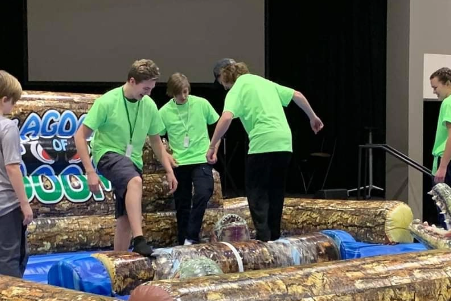 A group of people in green shirts are playing a game with logs.