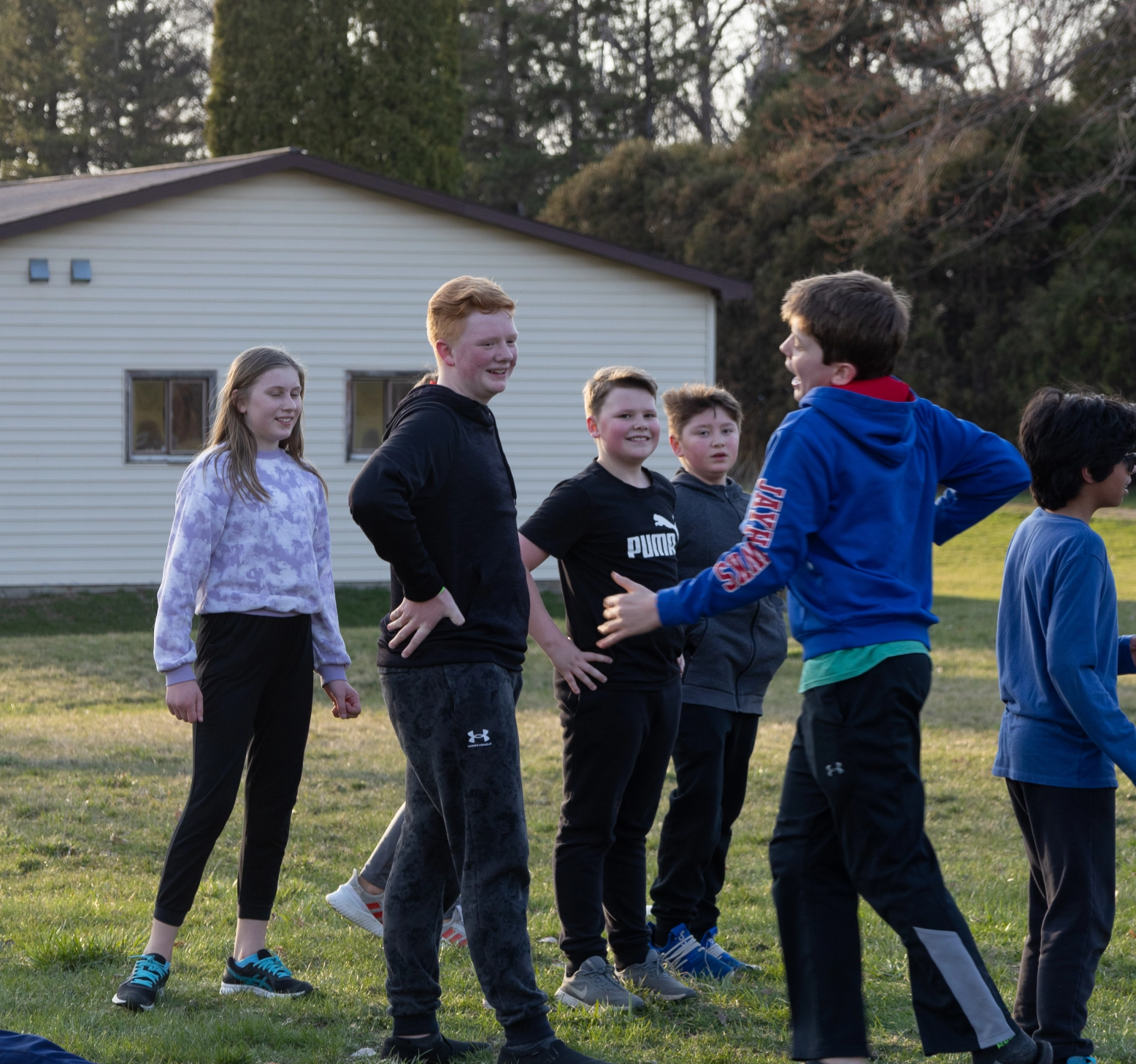 A group of kids are standing in a grassy field in front of a white house