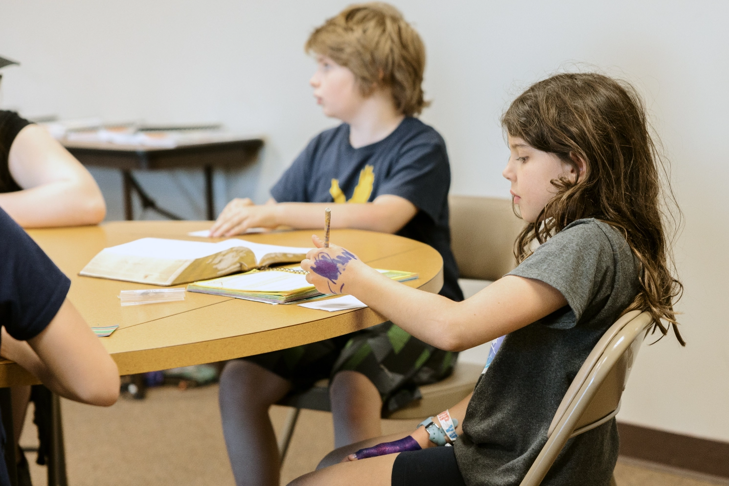 A group of children are sitting at a table with a bible.