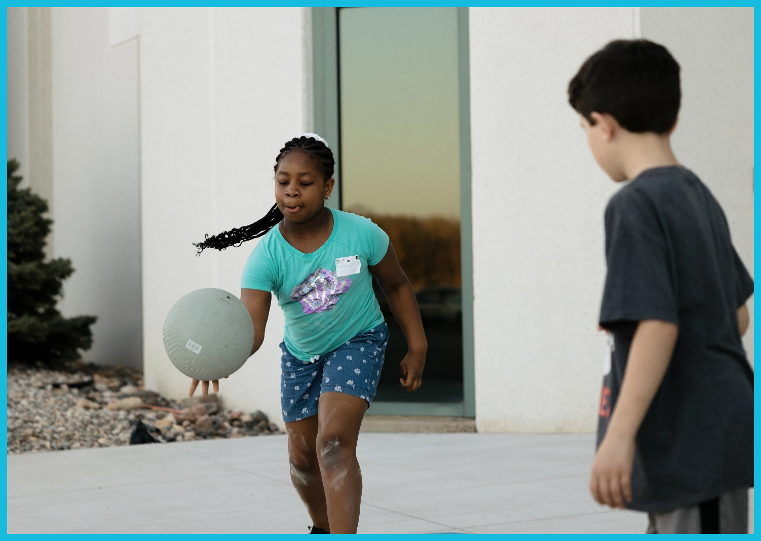 A boy and a girl are playing with a ball on the sidewalk.