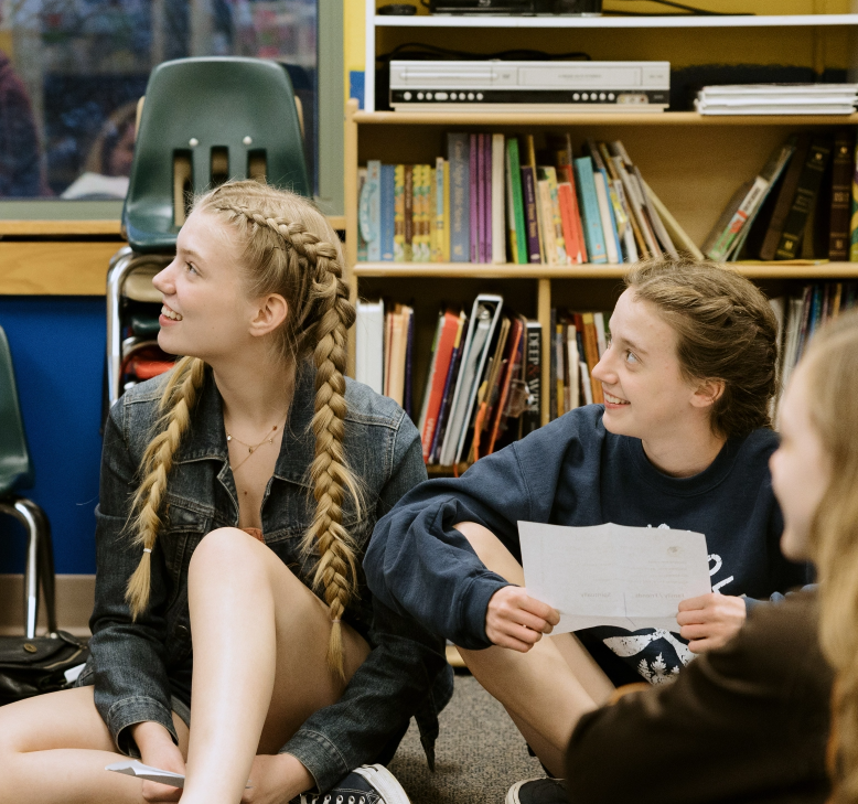 Three girls are sitting on the floor in front of a bookshelf