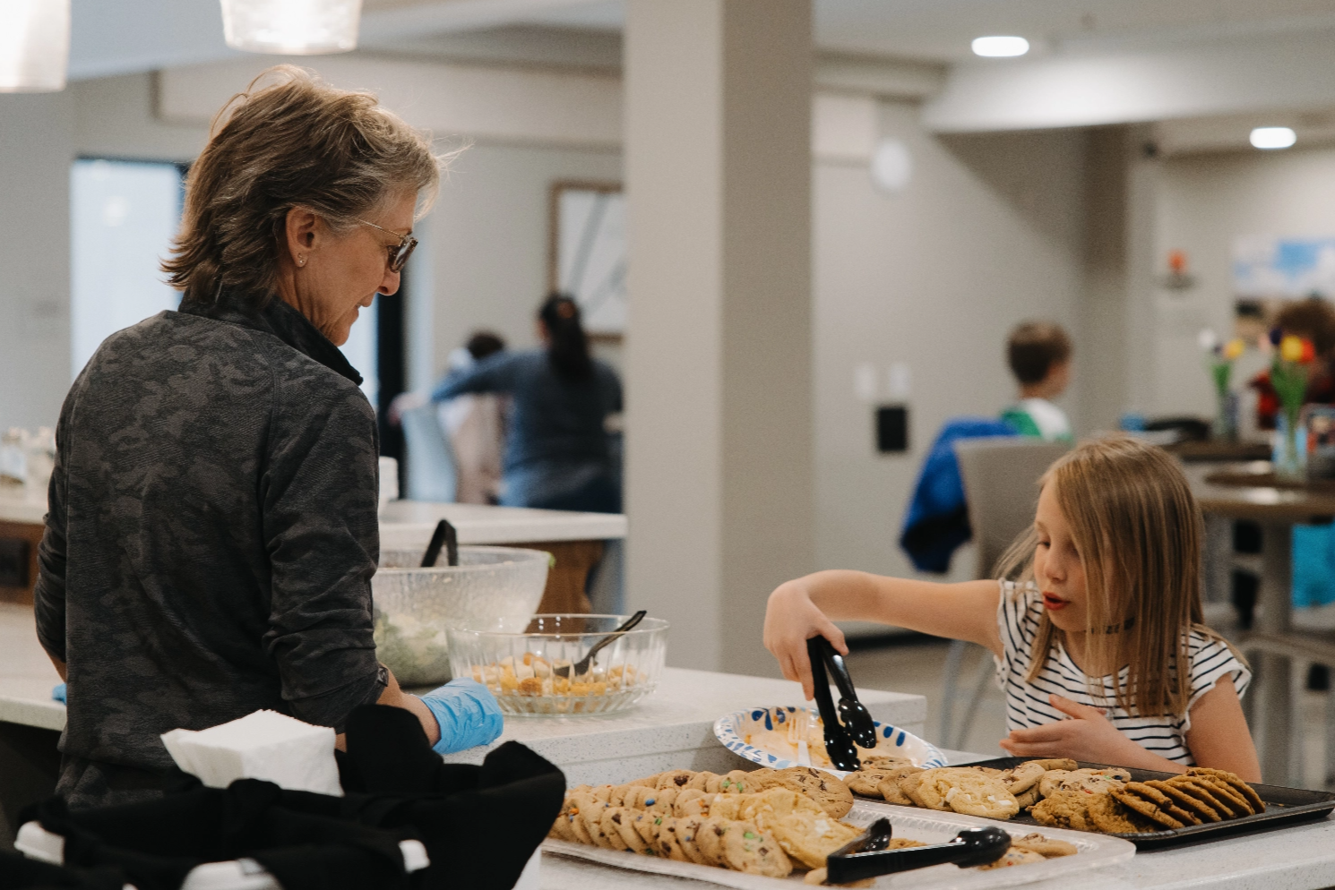 A woman and a little girl are sitting at a table making cookies.