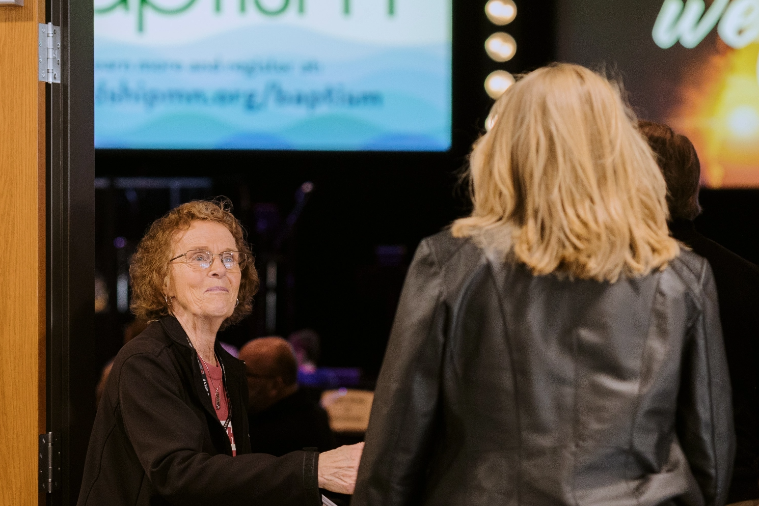 A woman in a black jacket is shaking hands with another woman.