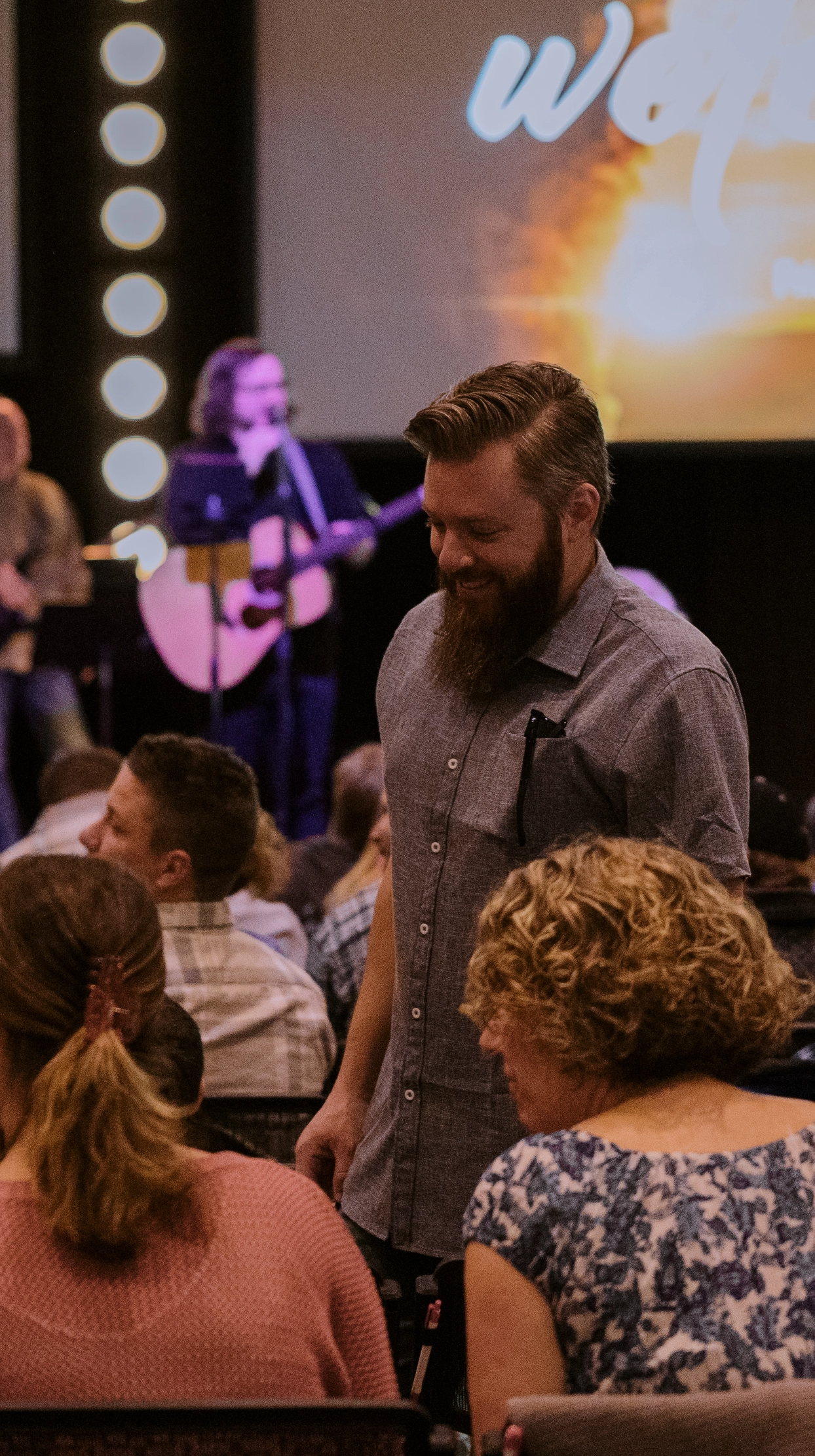 A man with a beard is standing in front of a group of people in a church.