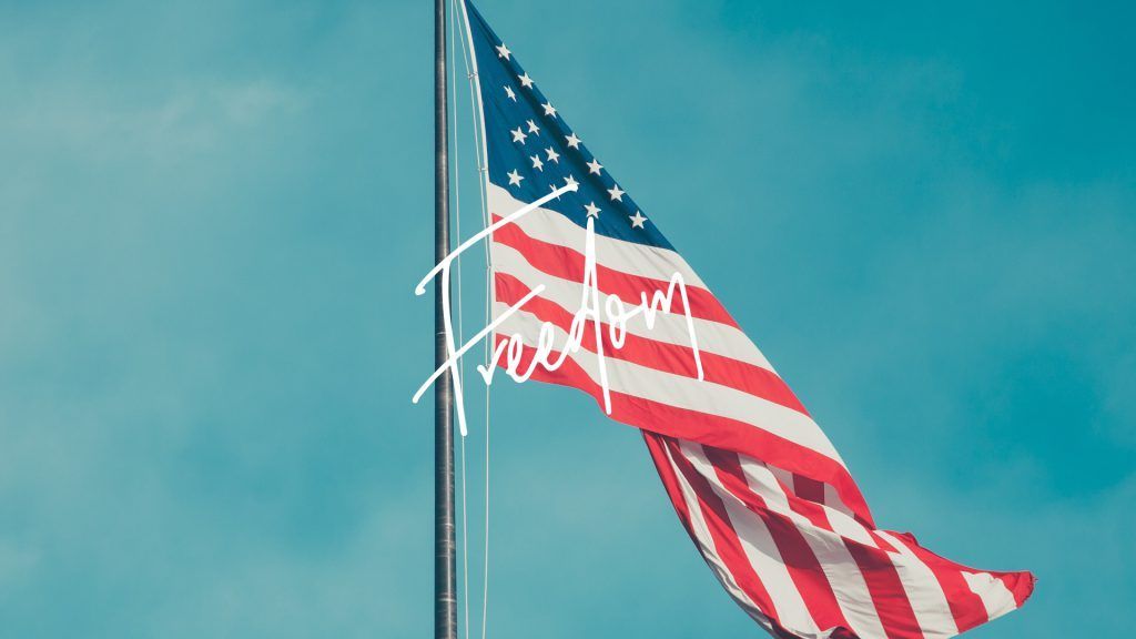 An american flag is waving in the wind against a blue sky.