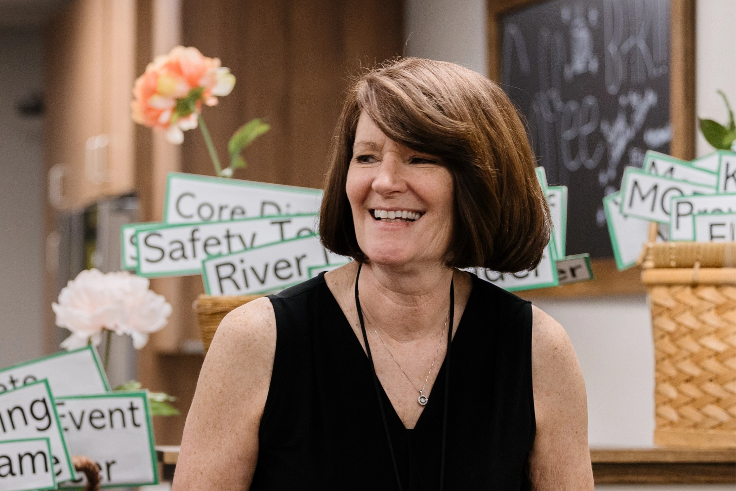 A woman is smiling while sitting in front of a chalkboard.
