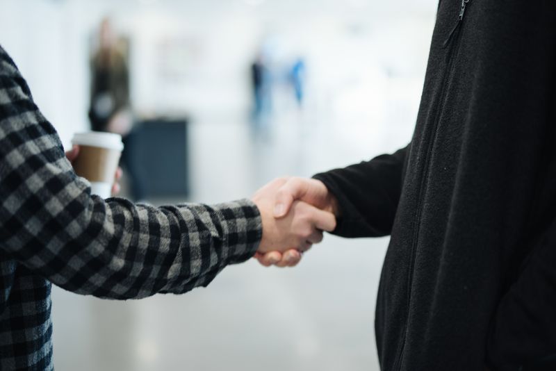 A man is shaking hands with another man while holding a cup of coffee.