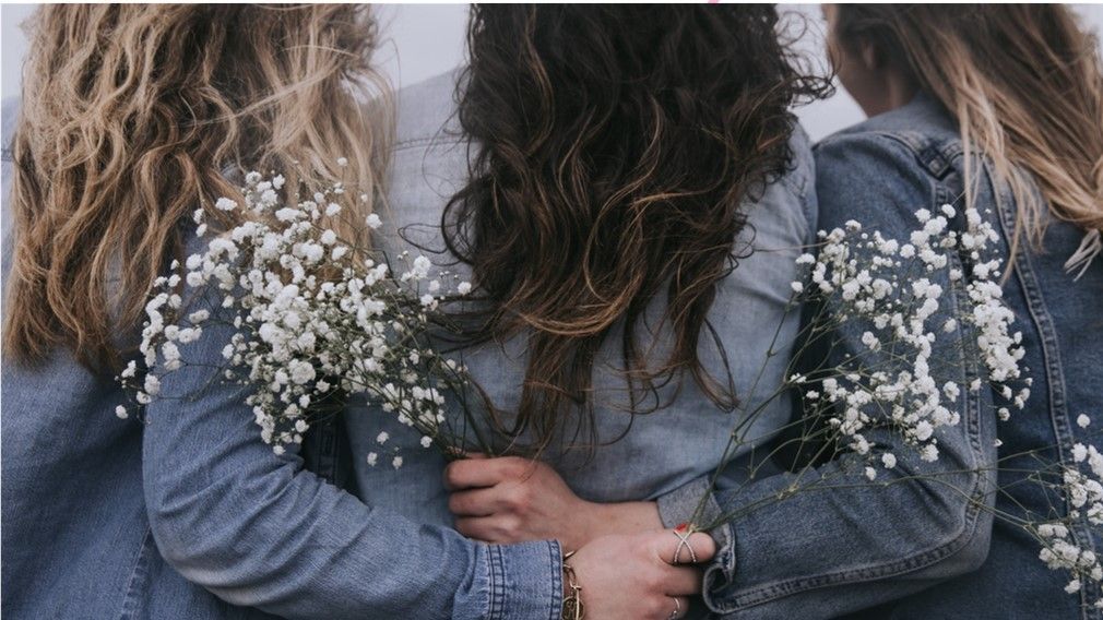 Three women are hugging each other while holding baby 's breath flowers.