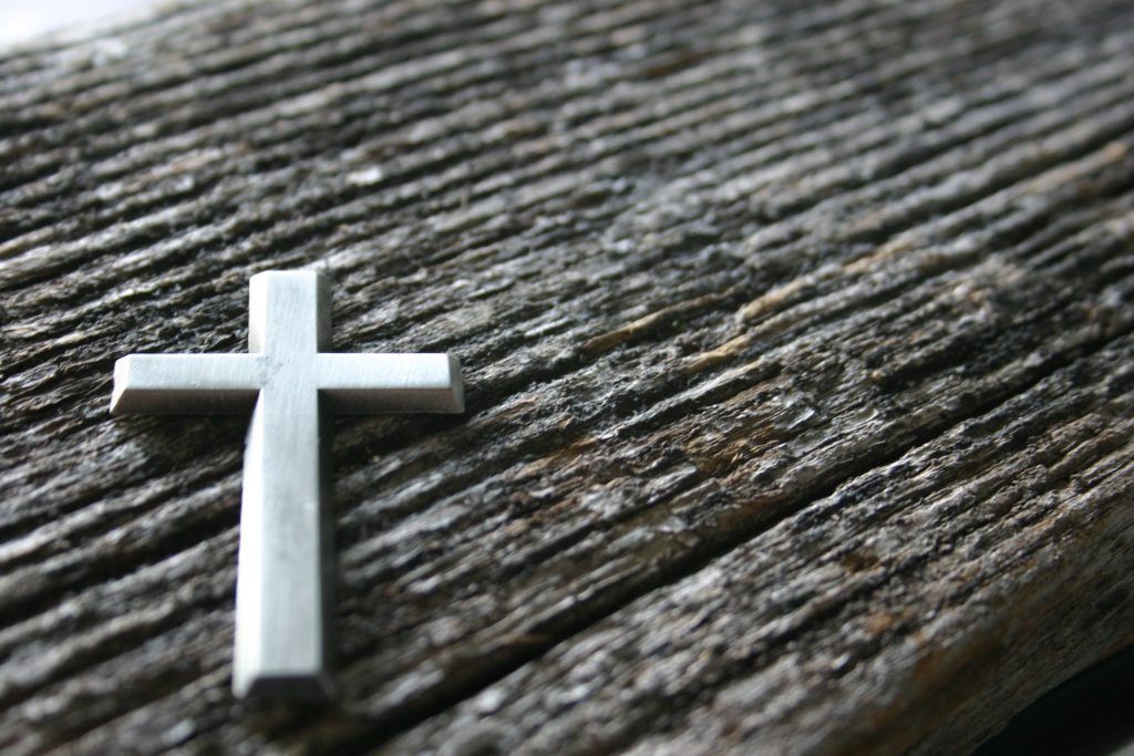 A small silver cross is sitting on a wooden surface.