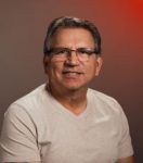 A man wearing glasses and a white shirt is smiling for the camera.