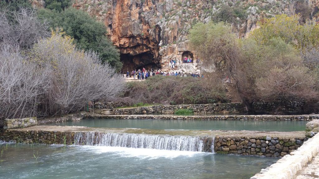 A river with a waterfall and a cave in the background