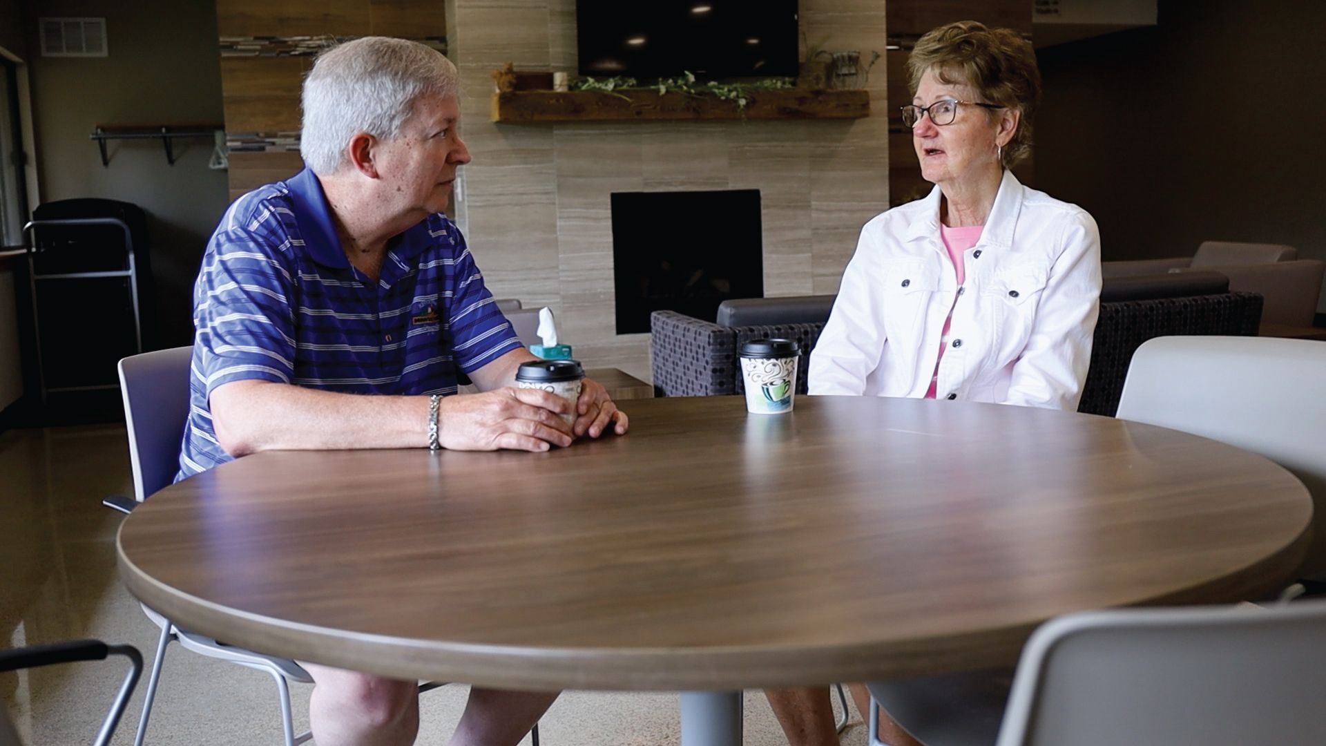 A man and a woman are sitting at a table talking to each other.