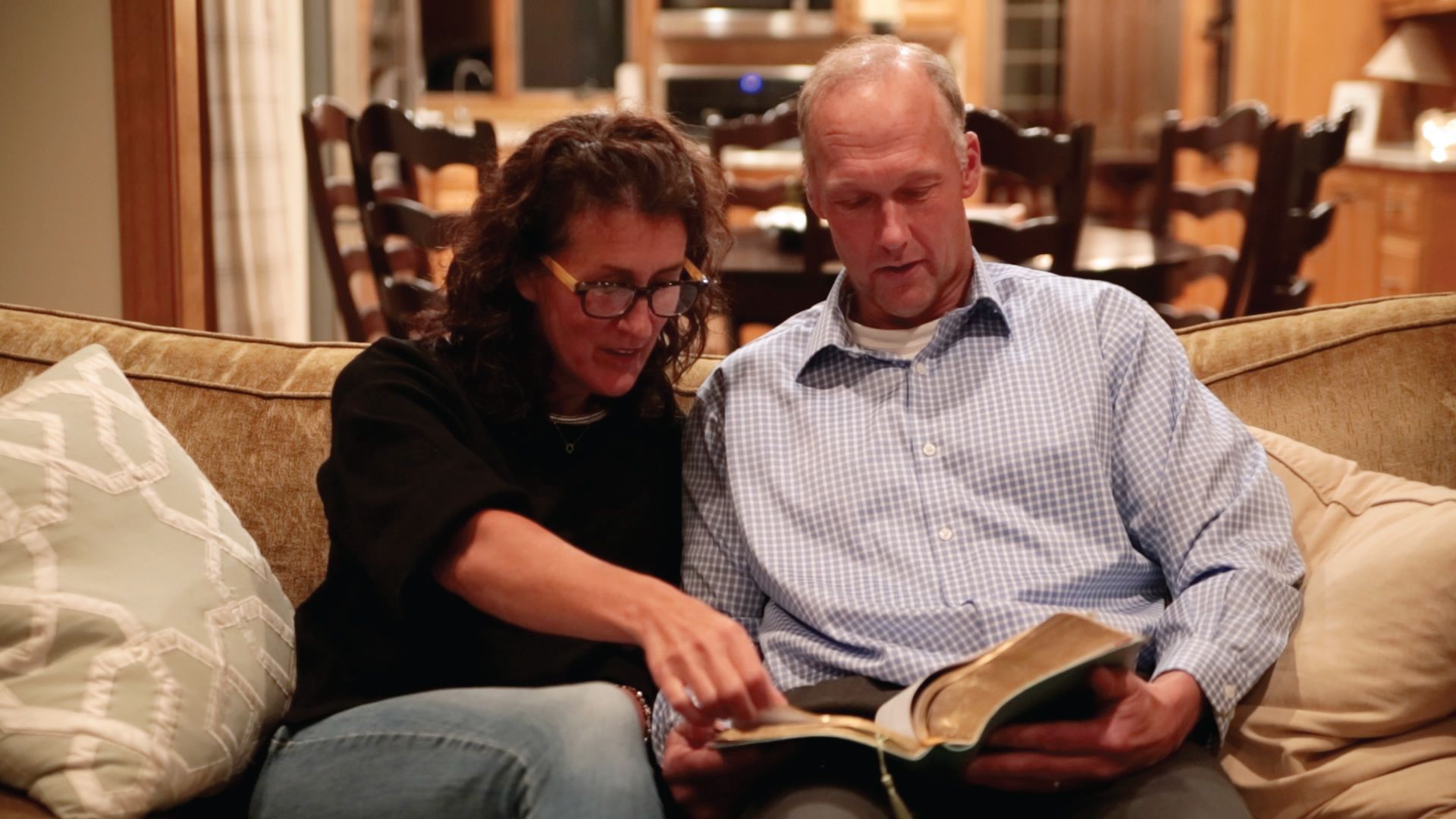 A man and a woman are sitting on a couch reading a bible.