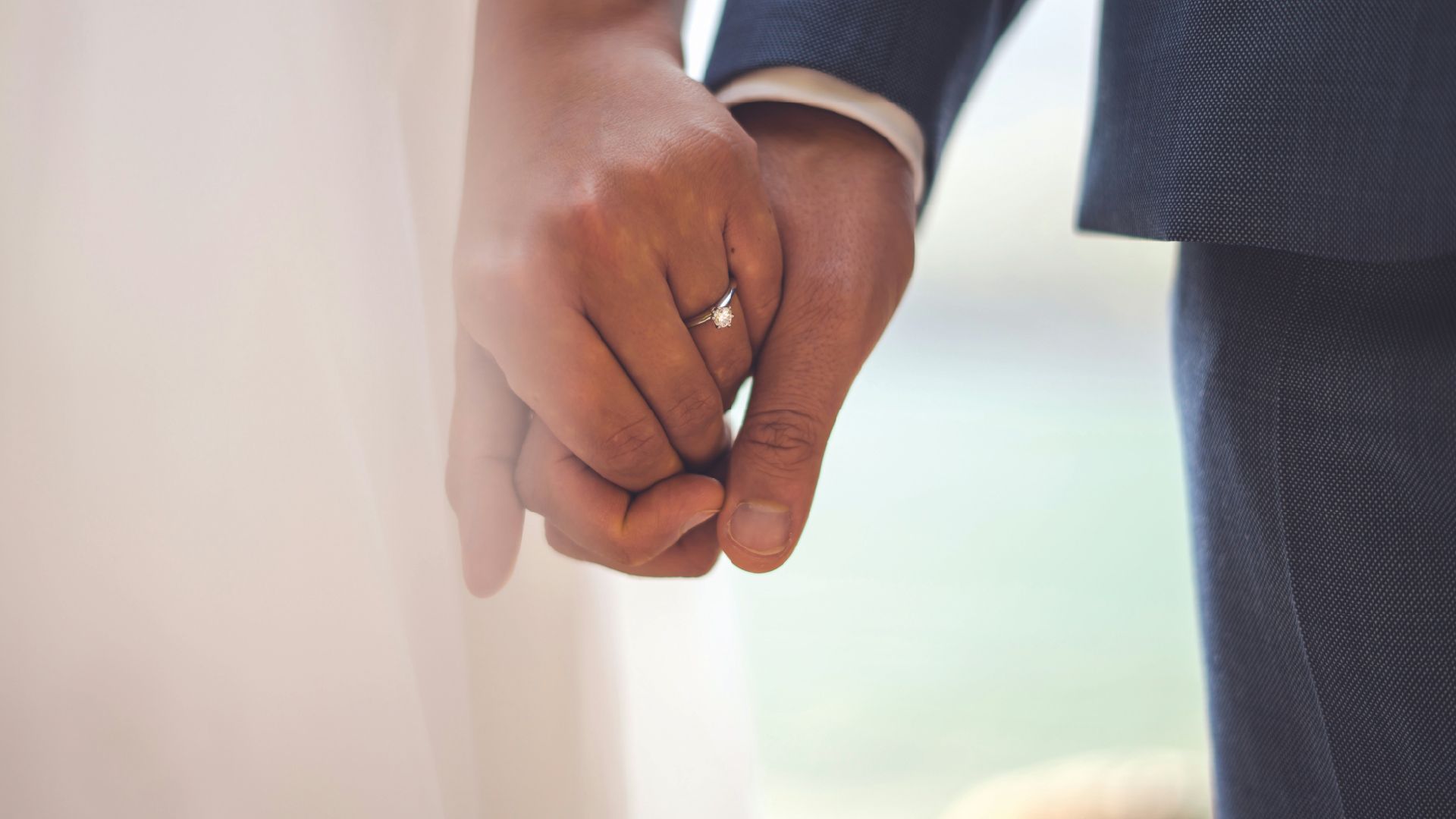 A bride and groom are holding hands with their wedding rings on.