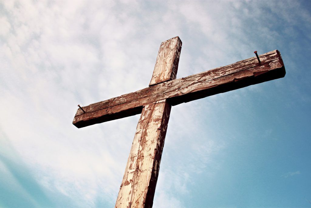 A wooden cross with nails in it is against a blue sky.