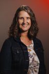 A woman in a denim jacket and floral shirt is smiling for the camera.