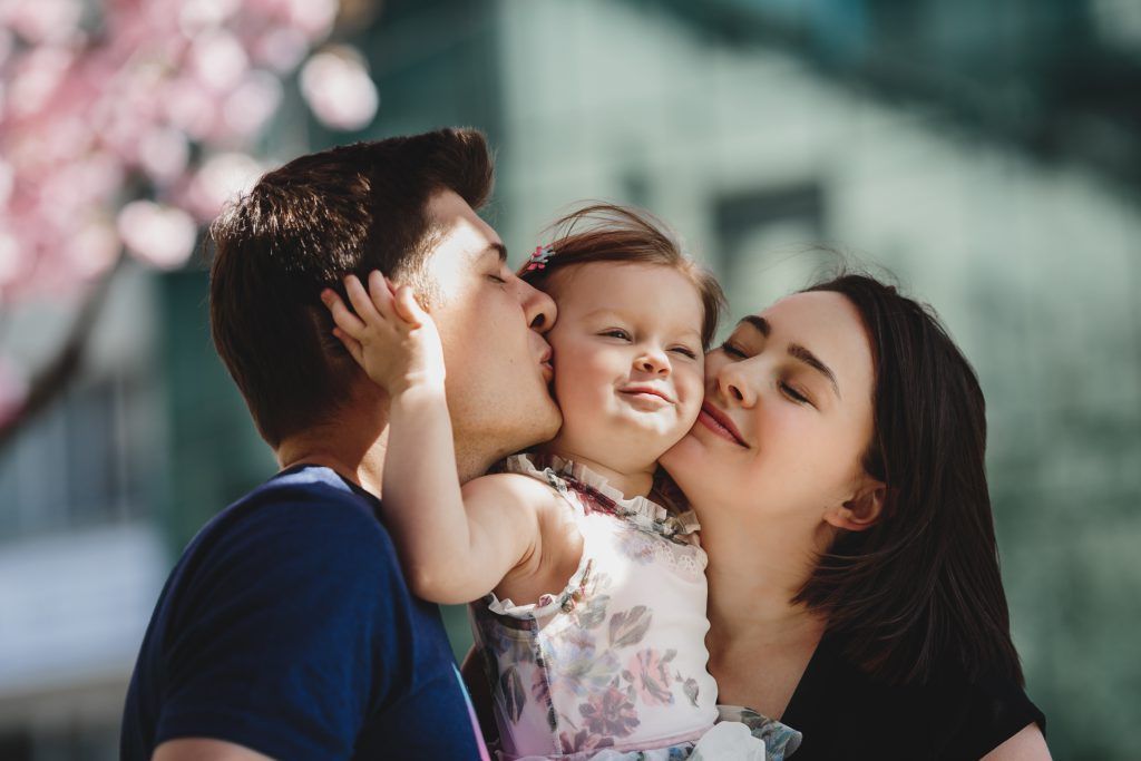 A man and woman are kissing a baby on the cheek.
