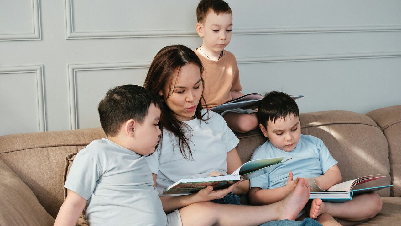 A woman is reading a book to three children while sitting on a couch.