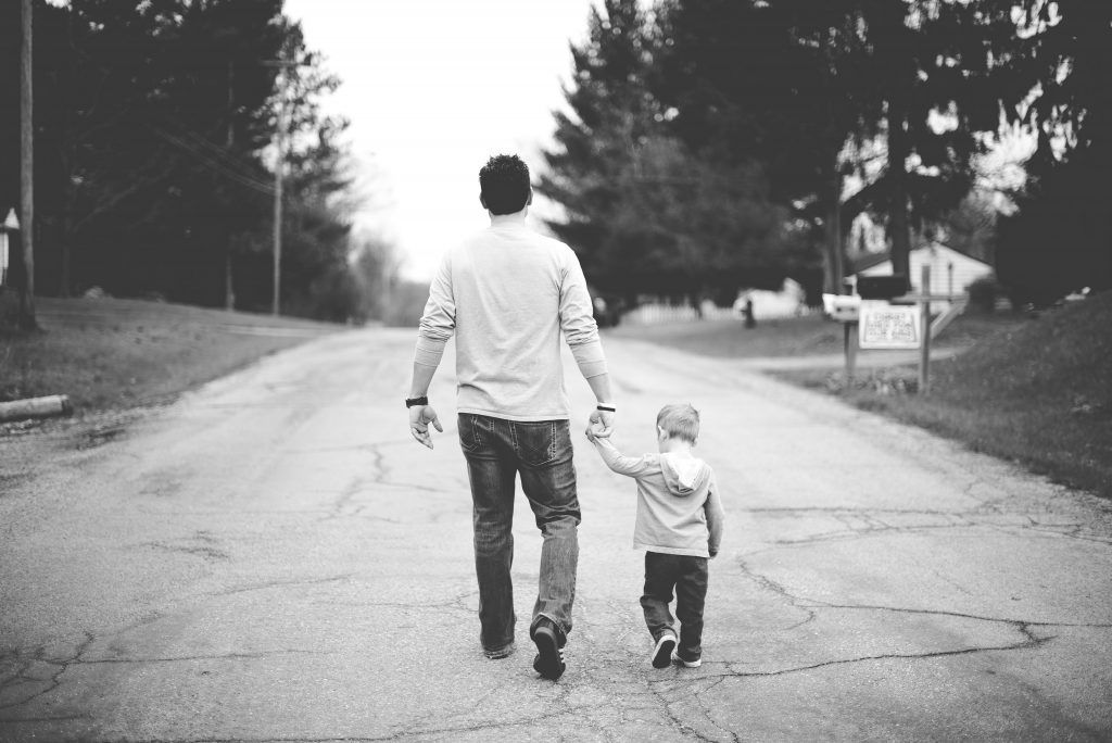 A man and a child are walking down a road holding hands.