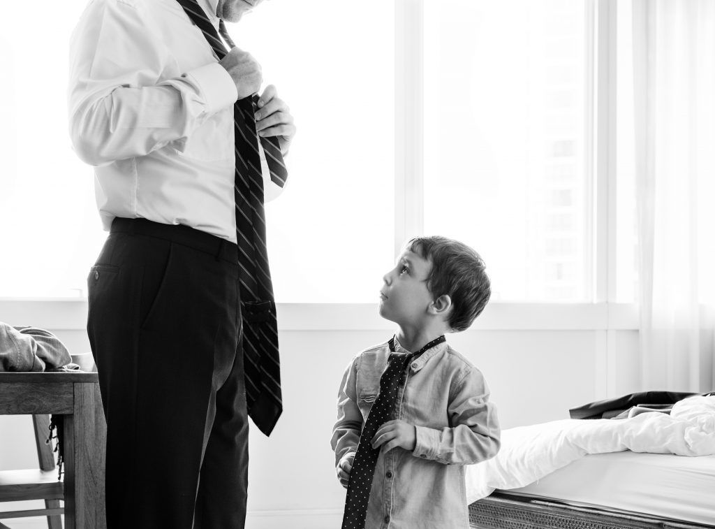 A man is helping a young boy tie his tie.