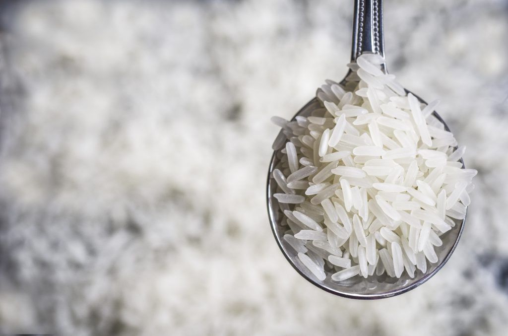A spoon filled with white rice is sitting on top of a pile of white rice.
